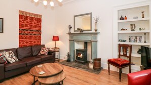Un salon avec une cheminée, un canapé, un fauteuil rouge, une table basse en bois et une bibliothèque.