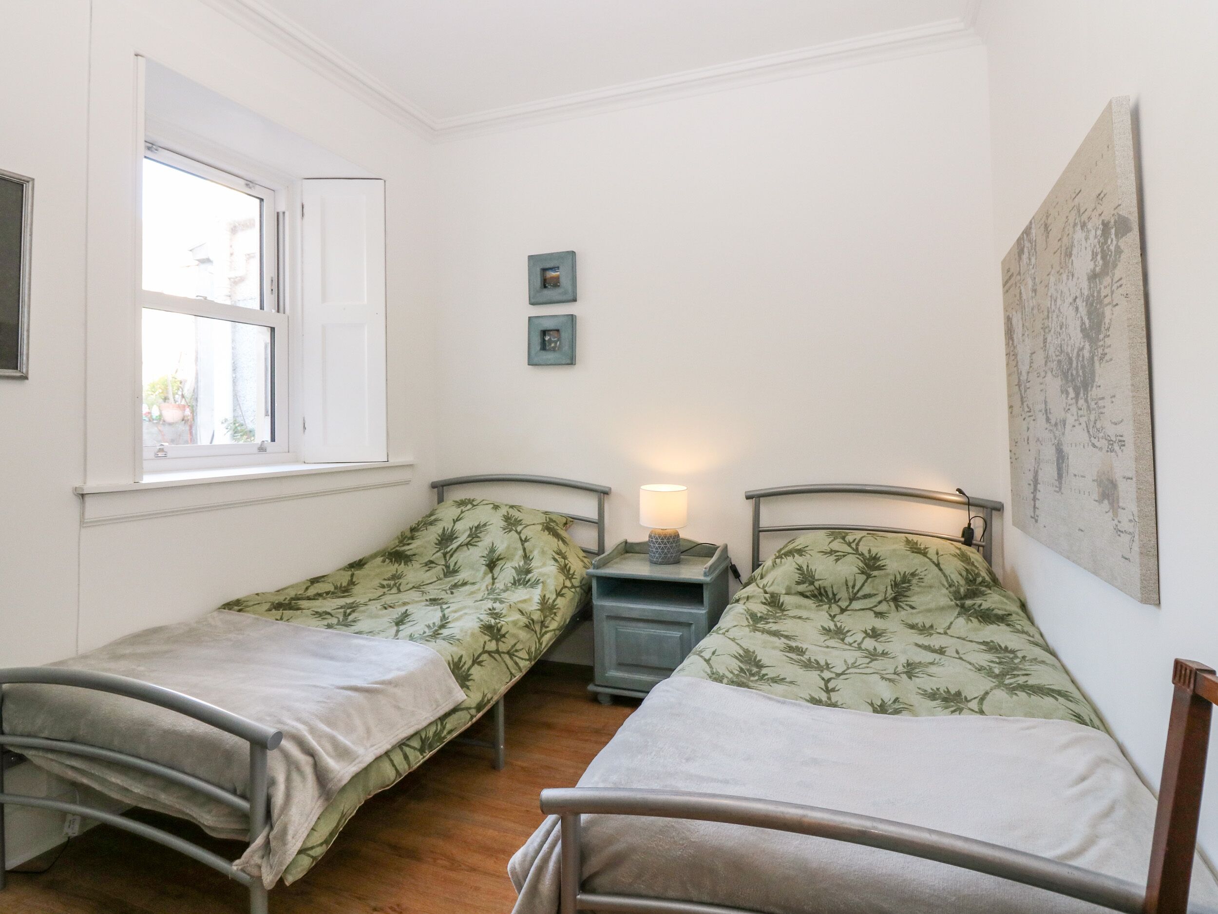 A small, clean room with two single beds, a window, a nightstand with a lamp, and a map on the wall.