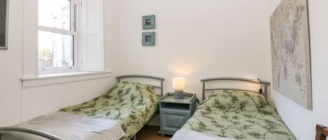 A small, clean room with two single beds, a window, a nightstand with a lamp, and a map on the wall.