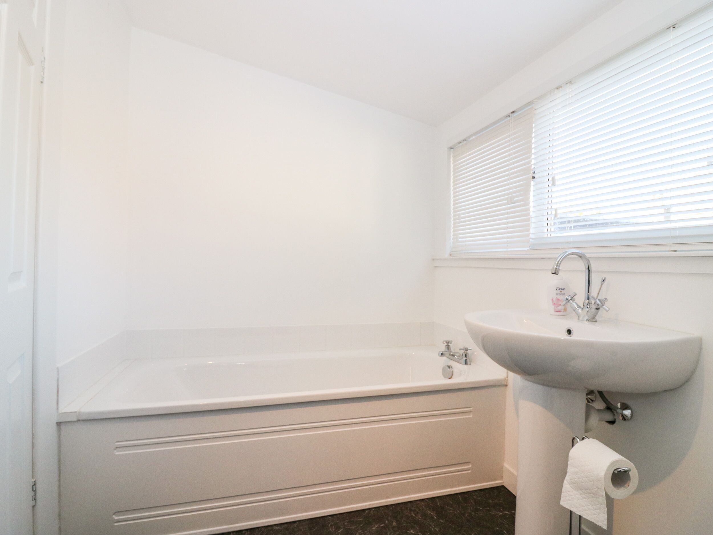 A bathroom with a bathtub, a sink, and a window with blinds.