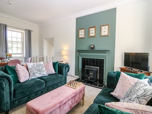 A living room with a fireplace, a television, and a chessboard on a pink ottoman. - South Stables - House Of Dun (Montrose)