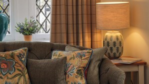 A cozy living room with a sofa, decorative pillows, a lamp, and a window with curtains. - East Lodge - Crathes Castle (Banchory)