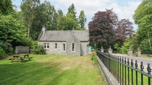 A stone building with a pitched roof, a picnic table, and a metal fence. - East Lodge - Crathes Castle (Banchory)