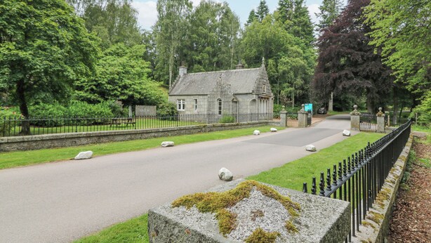 A stone building with a traditional design, surrounded by lush greenery and a paved road. - East Lodge - Crathes Castle (Banchory)