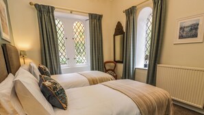 A double bed with white linens and decorative pillows, a wooden chair, a mirror, and a window with curtains. - East Lodge - Crathes Castle (Banchory)