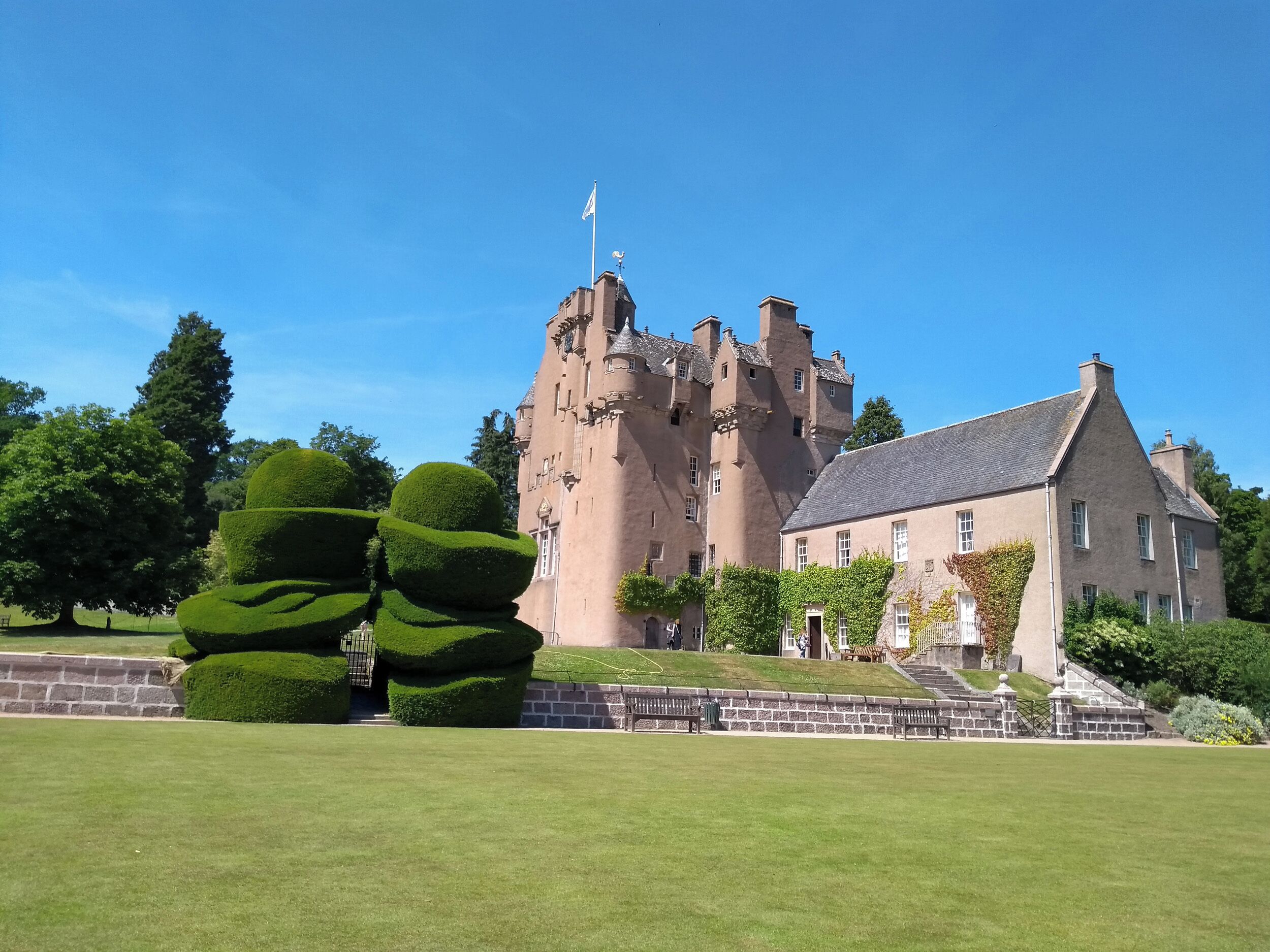 A castle with a prominent tower, a well-maintained lawn, and a clear blue sky.