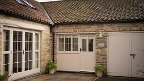 Un bâtiment en pierre avec un toit recouvert de tuiles, une porte blanche et une fenêtre.