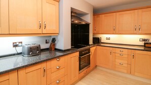 A modern kitchen with wooden cabinets, a built-in oven, a toaster, and a knife block. - Bolt's View (Bishop Auckland)