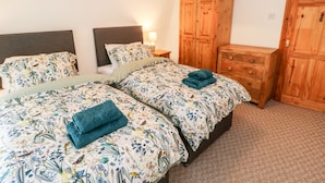 A bedroom with two beds, wooden wardrobe, and a nightstand with a lamp. - Bolt's View (Bishop Auckland)