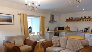 Una sala de estar acogedora con dos sofás de cuero marrón y un reposapiés a cuadros, una mesa de comedor y una zona de cocina con microondas y fregadero.