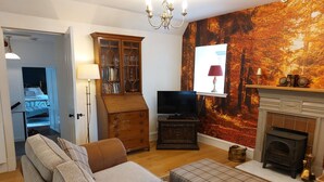 Sala de estar con sofá, reposapiés, televisor, estantería y chimenea.