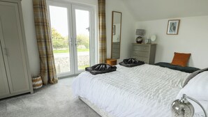 A bedroom with a large bed, a dresser, a mirror, and a view through the glass doors. - 4 Parc Delfryn (Brynteg)