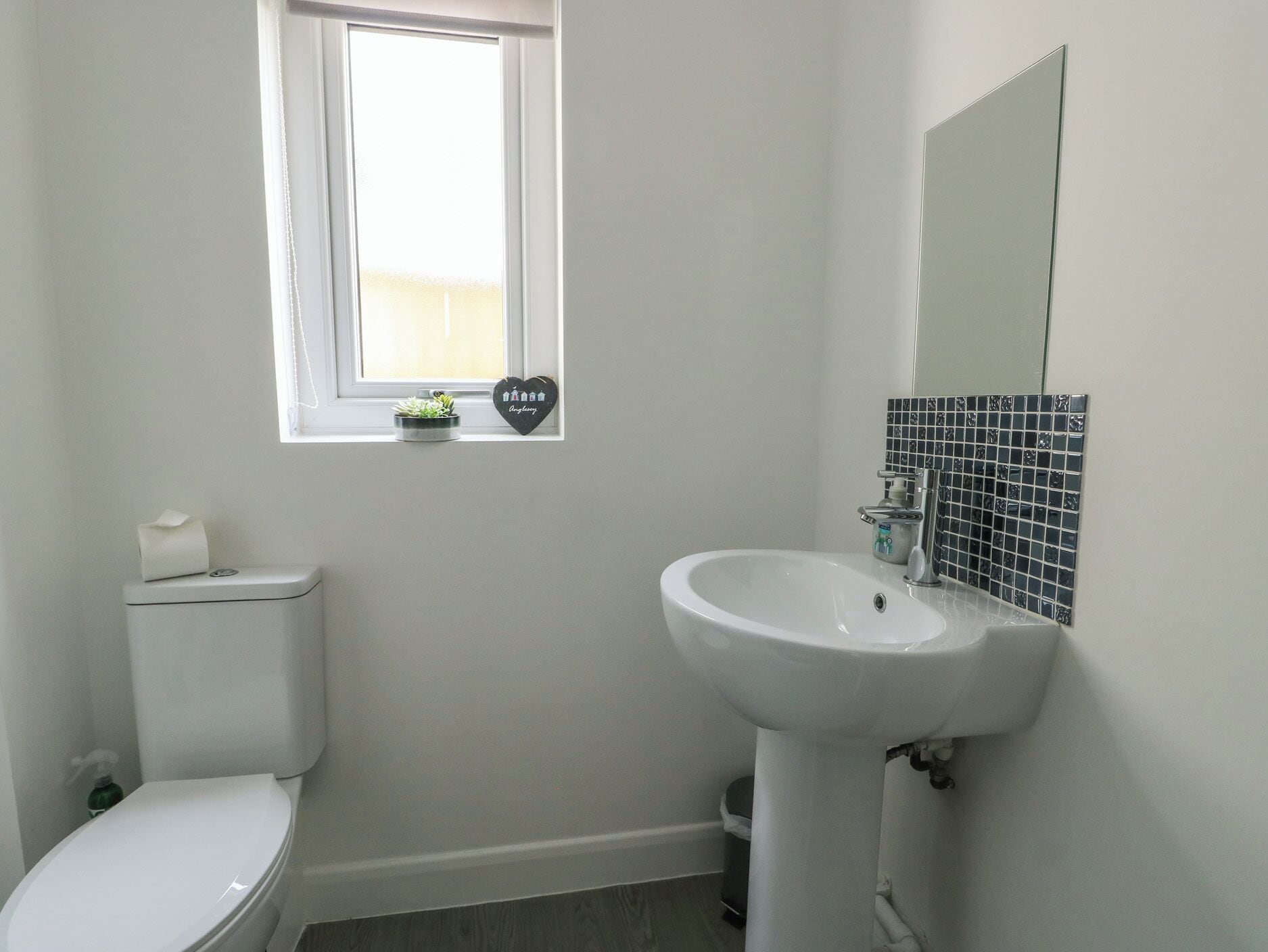 A bathroom with a toilet, sink, and a window above the sink.