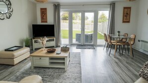 A modern living room with a flat-screen TV, a coffee table, sofas, and a dining area with chairs. - 4 Parc Delfryn (Brynteg)