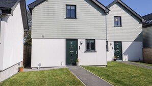 A modern two-story house with a grey exterior, a front entrance with a green door, and a small pathway leading to the entrance. - 4 Parc Delfryn (Brynteg)
