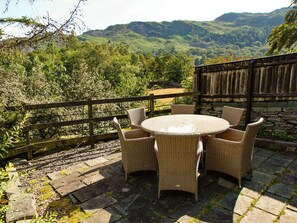 A round wicker table with six chairs on a stone patio, overlooking a lush valley with mountains in the background. - Plumblands (Ambleside)