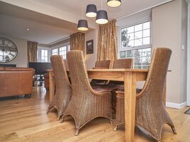 Un comedor con sillas de mimbre y una mesa de madera, ventanas grandes y un reloj en la pared.