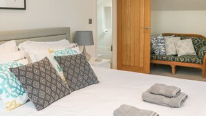 Une chambre d’hôtel bien aménagée, avec un lit, une table de chevet, une lampe, une armoire en bois et un canapé en osier agrémenté de coussins à motifs.
