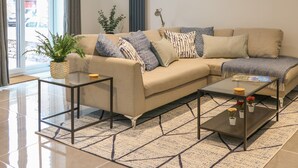 Un salon moderne avec un canapé beige, deux tables basses en verre, un tapis à motifs et une plante en pot.
