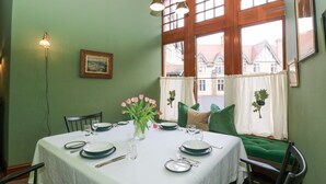 A dining room with a table set for four, green upholstered chairs, a vase with pink flowers, and a painting on the wall. - Derry - Mar Lodge Estate (Ballater)