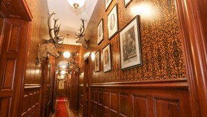 A hallway with wooden paneling, framed pictures on the walls, and antlers mounted on the ceiling. - Derry - Mar Lodge Estate (Ballater)