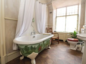 A bathroom with a vintage clawfoot bathtub, a wooden chair, a toilet, and a window with natural light.