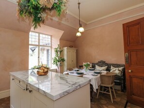 A kitchen with a marble countertop, a dining area with a table set for four, and a cozy seating area with a sofa and cushions.
