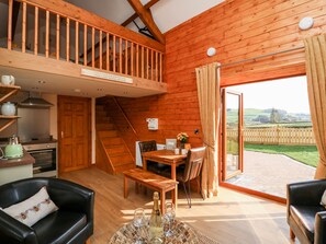 A cozy cabin interior with a wooden staircase, a dining area, and a view of the countryside. - Tegfan Barn (Rhayader)