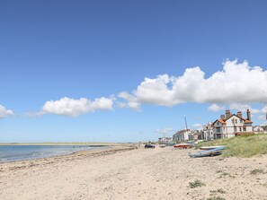 A beach with boats, a sandy shore, and houses in the background. - The Little Dolphins (Rhosneigr)