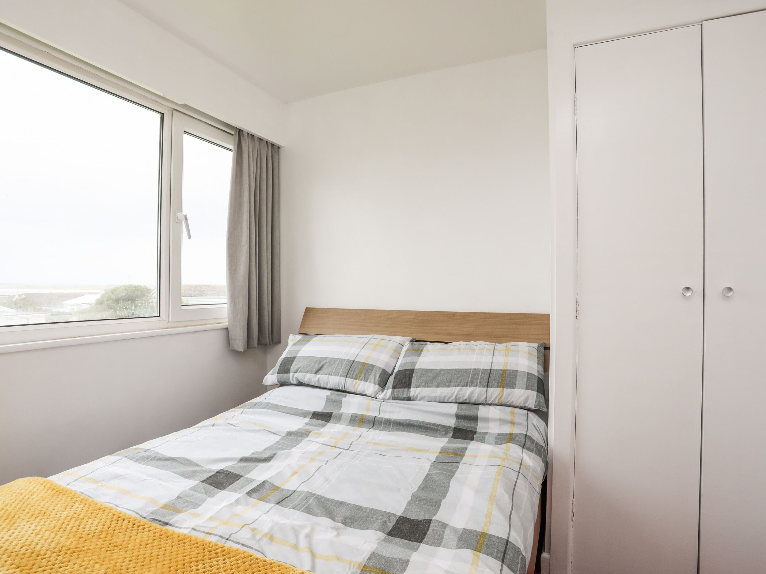 A bedroom with a bed, a window with curtains, and a wardrobe.