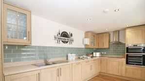 A modern kitchen with wooden cabinets, a stainless steel sink, and two built-in ovens. - Babbacombe Hall (Torquay)