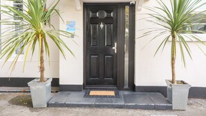 A black door with a white porch and two potted plants on either side. - Babbacombe Hall (Torquay)