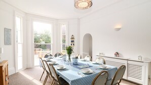 A dining area with a table set for six, white walls, a chandelier, and a view of the outdoors. - Babbacombe Hall (Torquay)