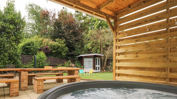 A hot tub under a wooden pergola in a backyard with picnic tables and a small shed. - Babbacombe Hall (Torquay)