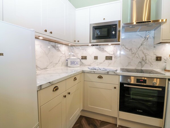 A modern kitchen with white cabinets, a microwave, a Bosch oven, and a bread container.