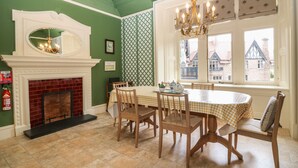 Una sala da pranzo con camino, pareti verdi, un lampadario e vista sugli edifici esterni.
