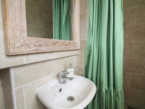 A bathroom with a white sink, a mirror with a wooden frame, and green curtains. - Bay Cosy (Pevensey)