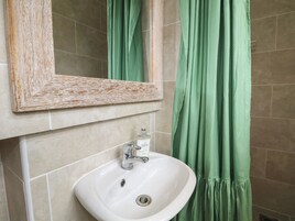 Un baño con lavamanos blanco, un espejo con marco de madera y cortinas verdes.