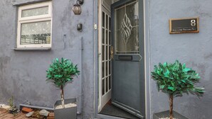 A building with a grey exterior, a door with a glass panel, a window, and two potted plants. - Bay Cosy (Pevensey)