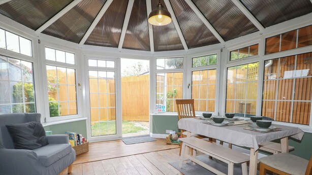 A conservatory with a wooden floor, a dining table set with bowls, and a grey sofa. - Bay Cosy (Pevensey)