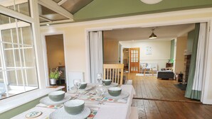A dining area with a table set for four, a wooden floor, and a view into another room with a fireplace. - Bay Cosy (Pevensey)