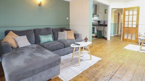 A living room with a grey sectional sofa, a small white side table, and a wooden floor. - Bay Cosy (Pevensey)