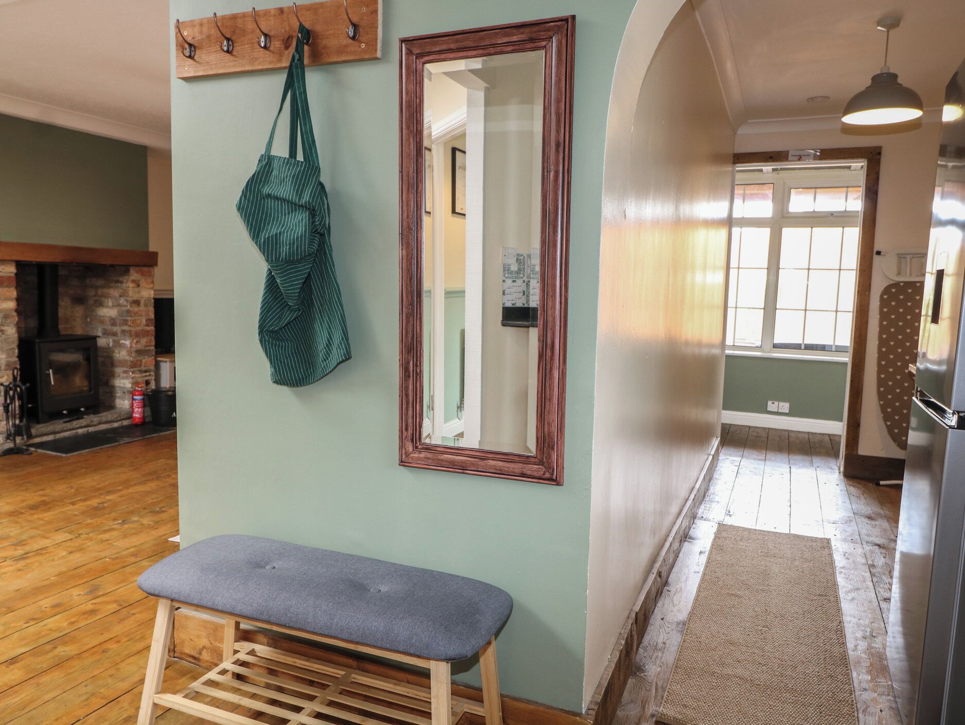 A room with a bench, a mirror, a coat rack, a fireplace, and a view of another room through an archway.