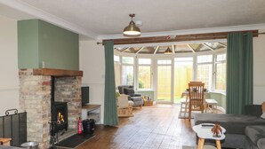 A living room with a fireplace, wooden flooring, a sofa, a table, and a view through large windows. - Bay Cosy (Pevensey)