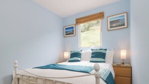 A neatly arranged bedroom with a bed, bedside tables, and a window with blinds. - Gecko Beach (Truro)