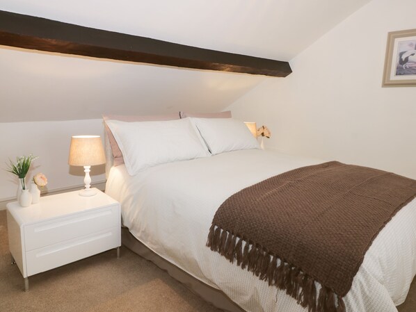 A bedroom with a bed, nightstands, a lamp, a vase with flowers, and a framed picture on the wall.