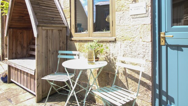 A rustic stone building with a wooden porch, a window, and a blue door. - Foxholes Barn (Kidderminster)