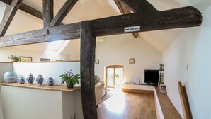 A wooden staircase with a 'MIND YOUR HEAD' sign, leading to a living area with a TV, books, and decorative items. - Foxholes Barn (Kidderminster)