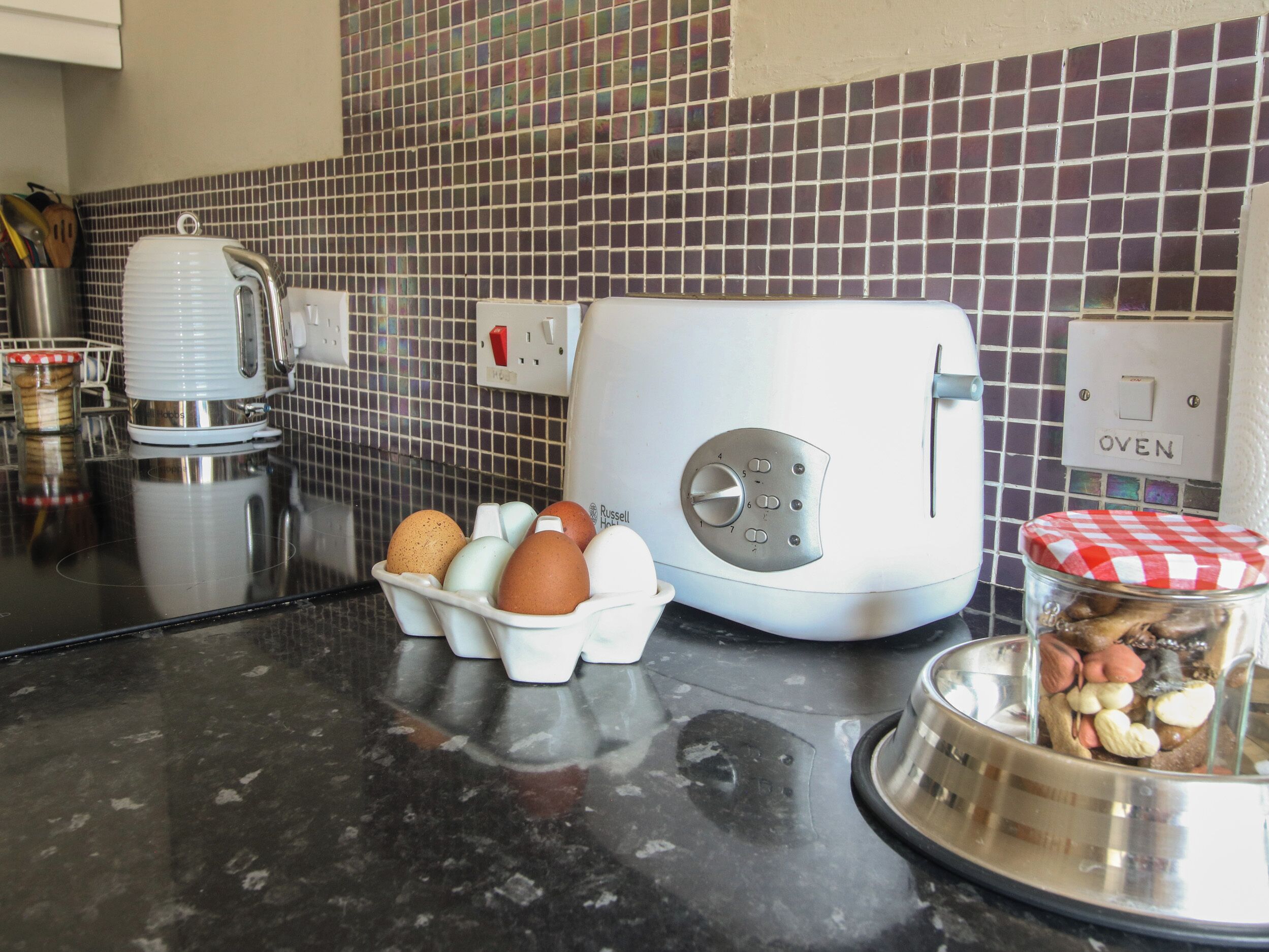 A kitchen with a toaster, a kettle, and a bowl of eggs on the counter.