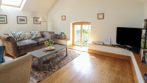 A spacious living room with a high ceiling, a large window, a sofa set, a coffee table, a TV, and a bookshelf. - Foxholes Barn (Kidderminster)